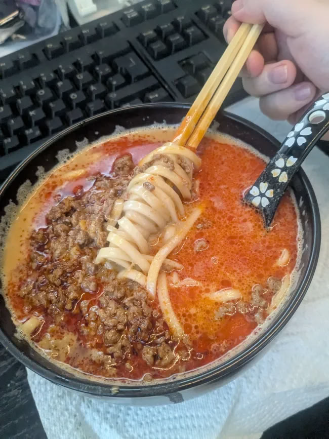 a bowl of ramen. a creamy red-ish broth with noodles and fried minced meat are in the soup